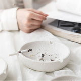 White ceramic face ashtray on a table, lifestyle photo with hand and cigarette