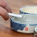 Blue and white ceramic ashtray in use with a cigarette, showing deep bowl and side cigarette rest