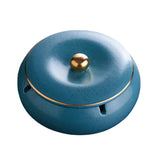 Teal blue covered ceramic ashtray with gold knob and cigarette rest on white background