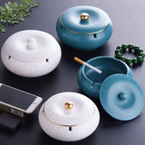 White and teal ceramic ashtrays with matching lids arranged on a dark tabletop