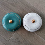Teal and white covered ceramic ashtrays displayed side by side on a wooden tabletop