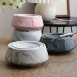 Pink, light gray, and dark gray marble-style ceramic ashtrays on tabletop