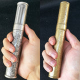 Hand holding engraved metal cigar tubes in silver and gold finishes