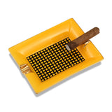 Yellow ceramic cigar ashtray with gold rests and cigar on white background