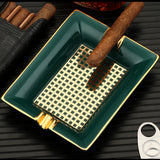 Teal ceramic cigar ashtray with gold cigar rests on black tabletop