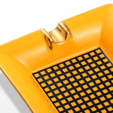 Close-up of yellow ceramic cigar ashtray with gold rest and patterned basin