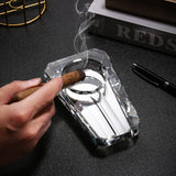 Hand holding clear crystal glass cigar ashtray beside cigar accessories on dark tabletop