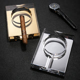 Amber gold and clear crystal glass cigar ashtrays with cigar and accessory on dark tabletop