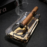 Amber gold crystal glass cigar ashtray with cigar and smoke on glossy dark tabletop