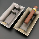 Silver rectangular metal cigar ashtray with cigar on dark background