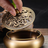 Retro copper ashtray with carved lid being lifted by hand to show the inside