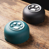 Cat ashtray with bottom part shown beside black round ashtray on wooden table